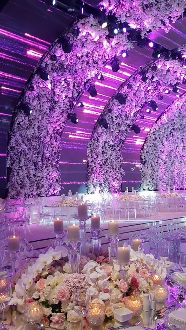 Curved floral arches with purple lighting over a wedding table with candles.
