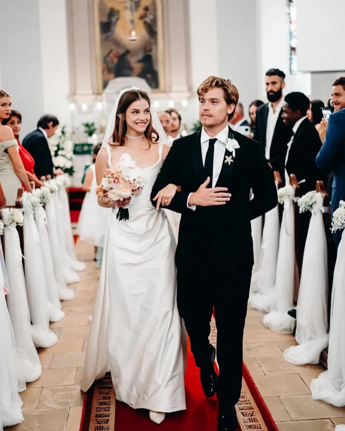 Bride in white wedding gown and groom in black tuxedo walking down church aisle