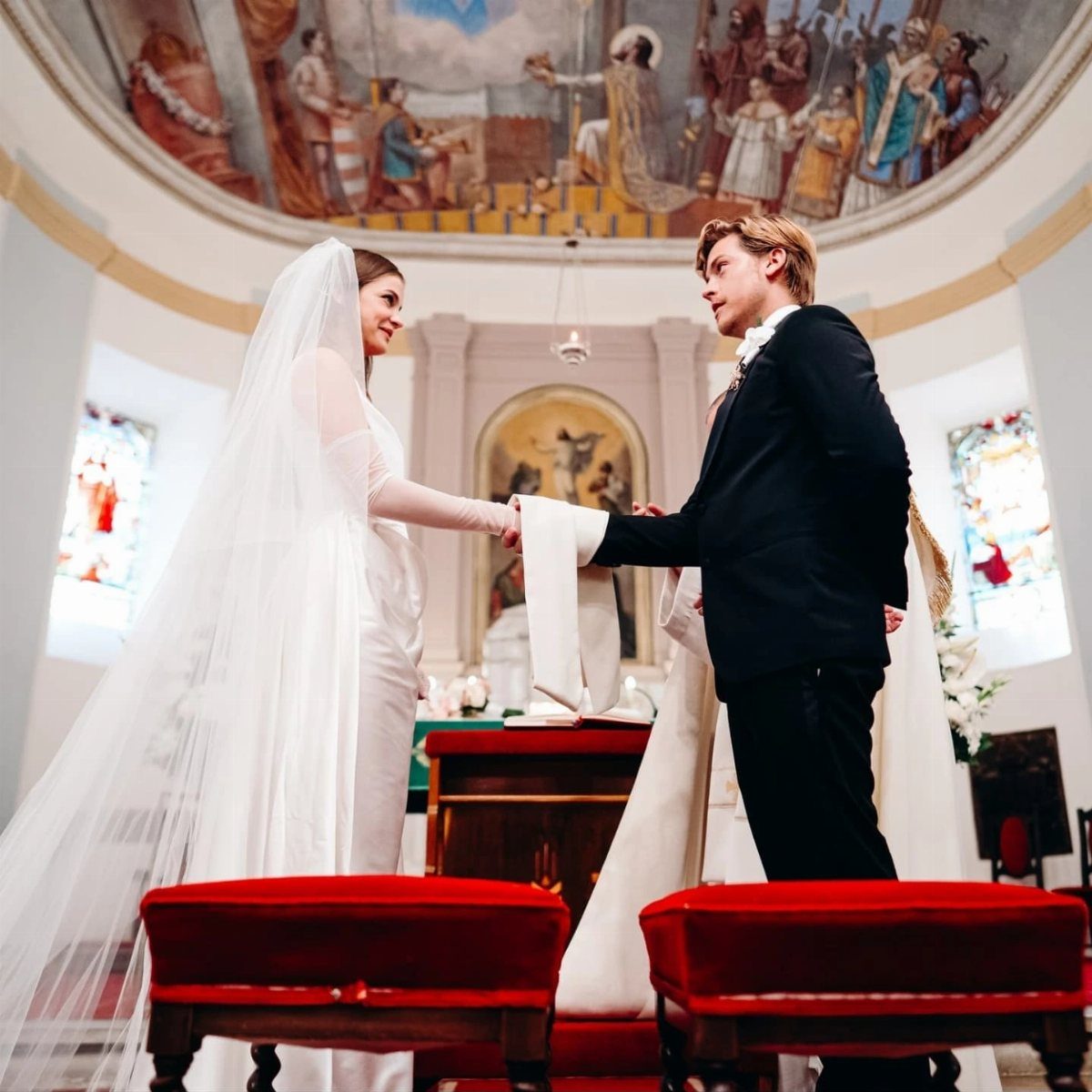 Bride in white gown and groom in black tuxedo holding hands in church