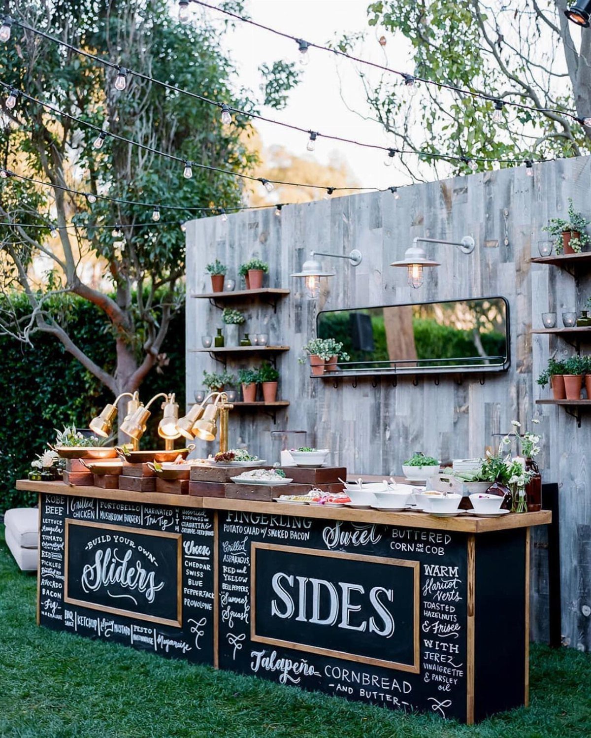Outdoor BBQ food station with chalkboard menu and rustic wooden fence backdrop