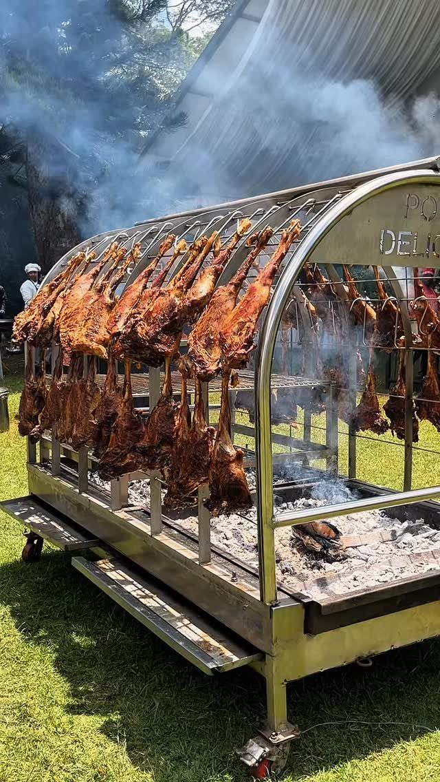 Whole lambs roasting on a large stainless steel outdoor grill over hot coals.