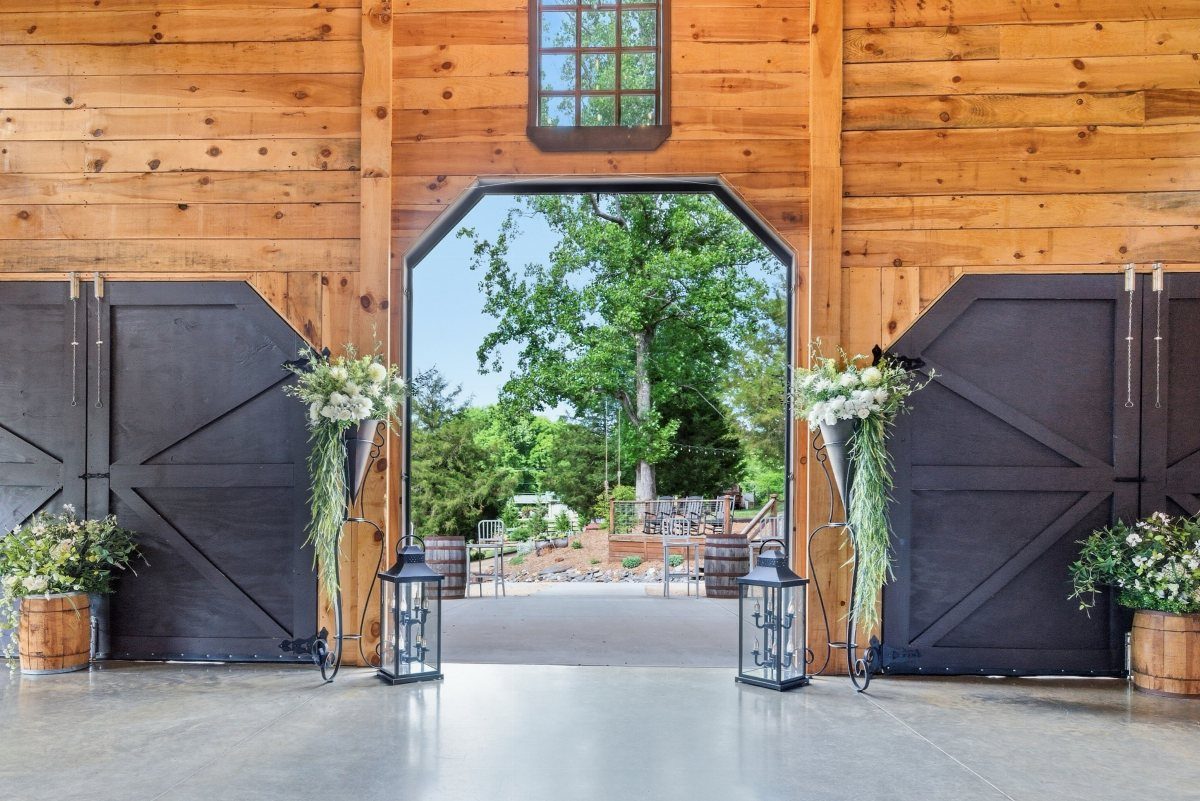 Open black barn doors with white floral arrangements and lanterns leading outdoors.