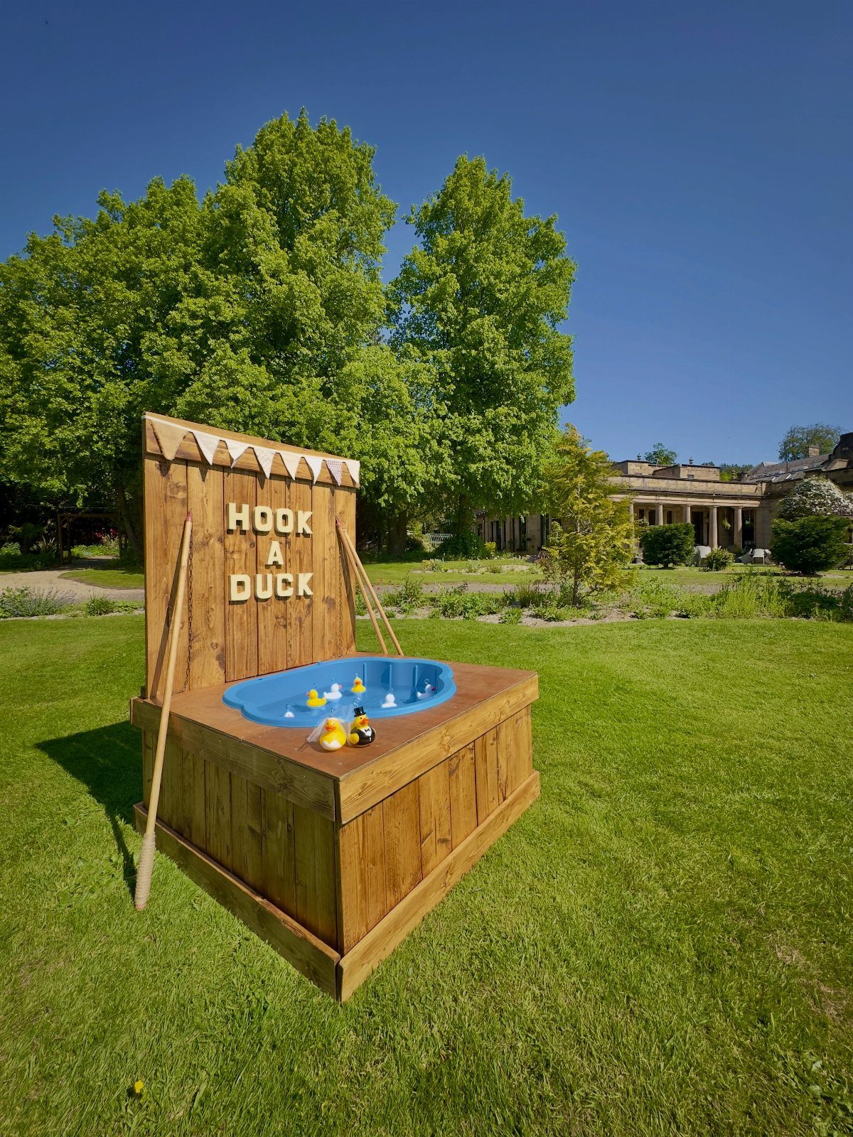 Wooden Hook a Duck game stand with blue tub on a sunny green lawn.
