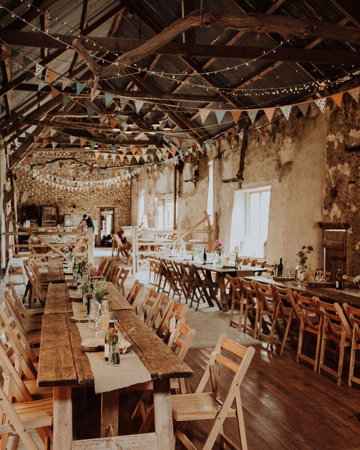 Rustic barn interior with long wooden tables, folding chairs, and festive bunting flags.