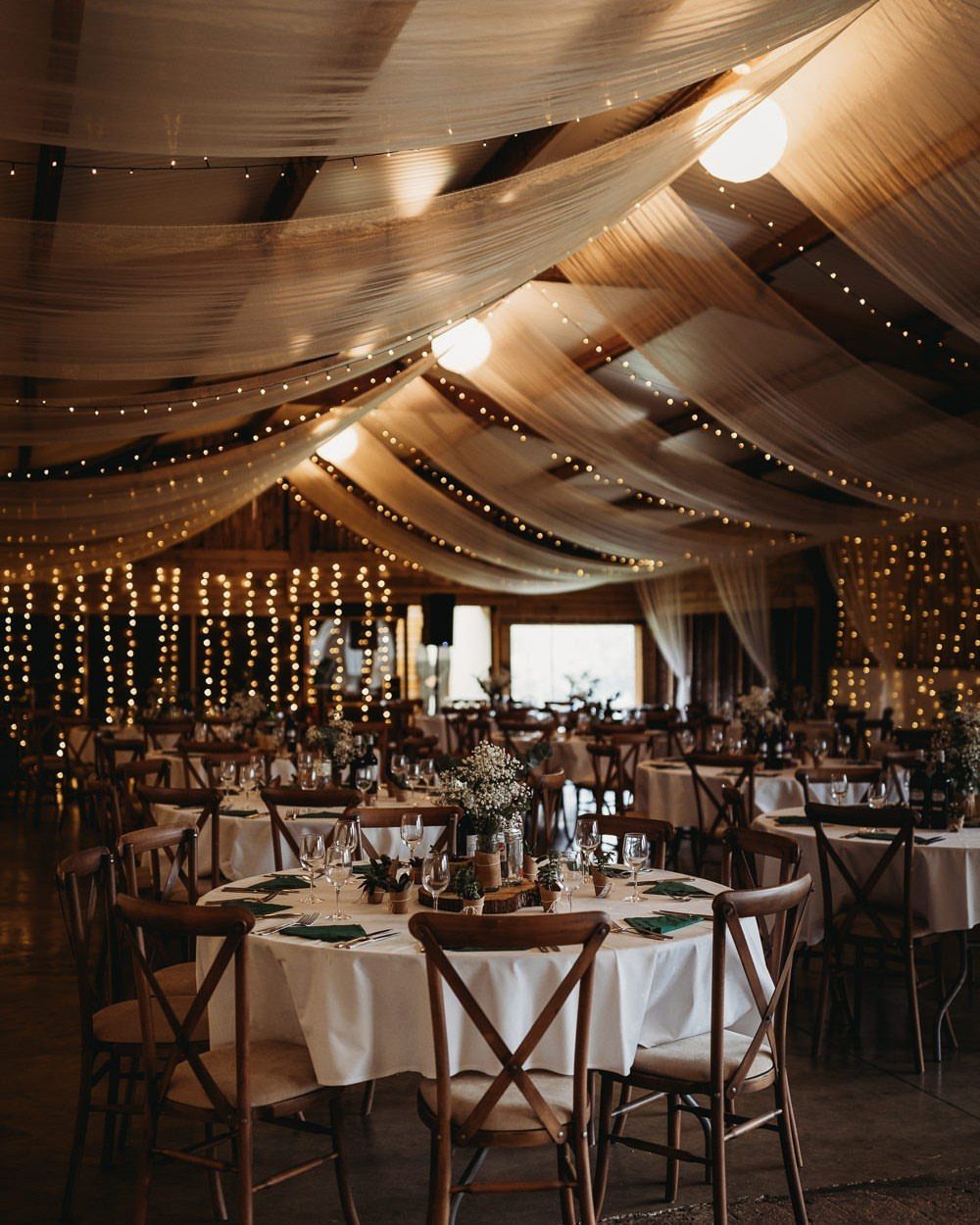 Barn wedding reception with draped ceiling fabric and warm glowing string lights