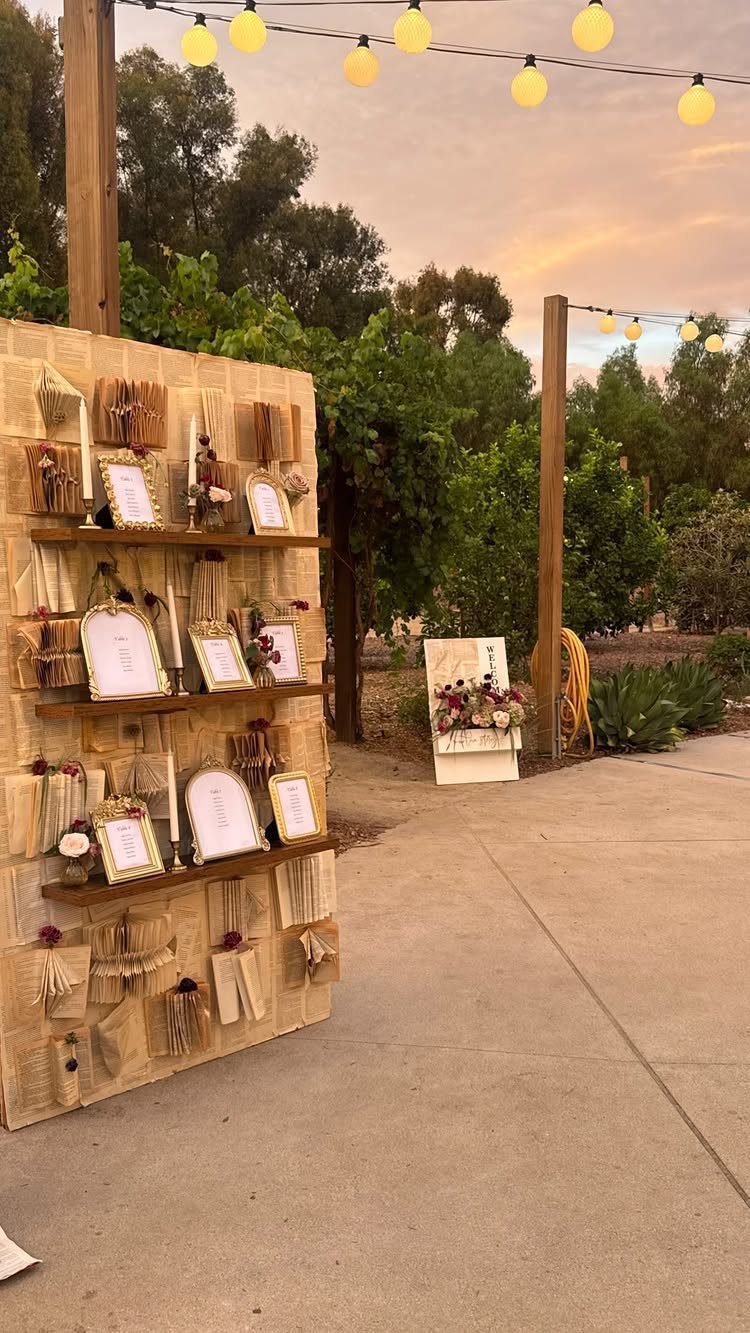 Wooden wall display with vintage books, framed photos, and overhead string lights outdoors.