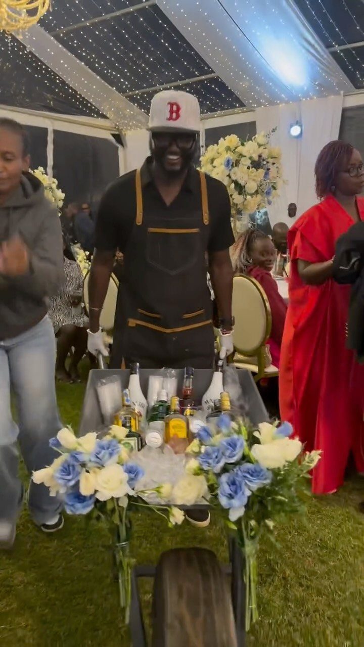Wheelbarrow bar with liquor bottles and blue flowers at an outdoor event.