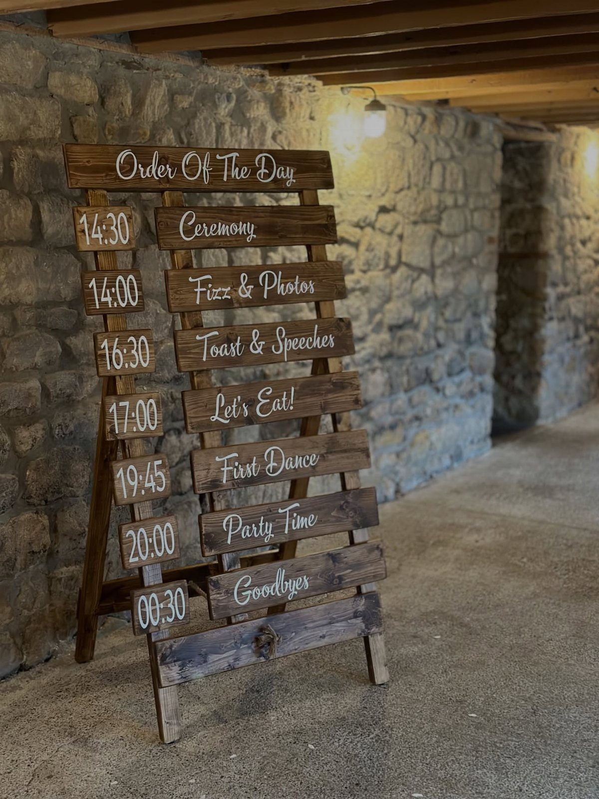 Wooden order of the day sign with white text against a stone wall