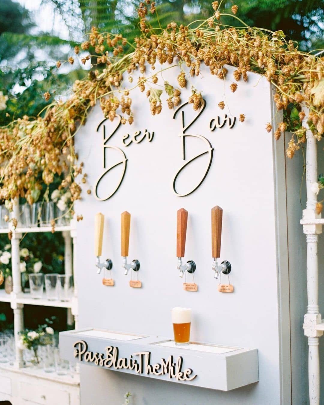 Beer bar station with four wooden taps, gold lettering, and dried floral decorations.