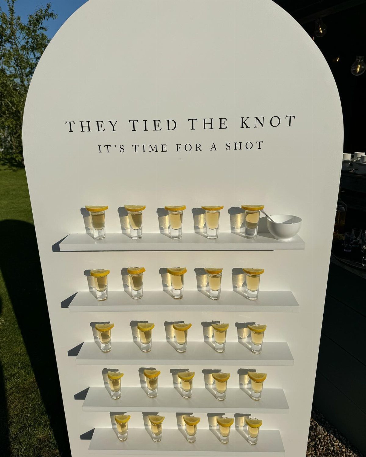 White arched shot glass display with yellow drinks and lemon garnishes for weddings.