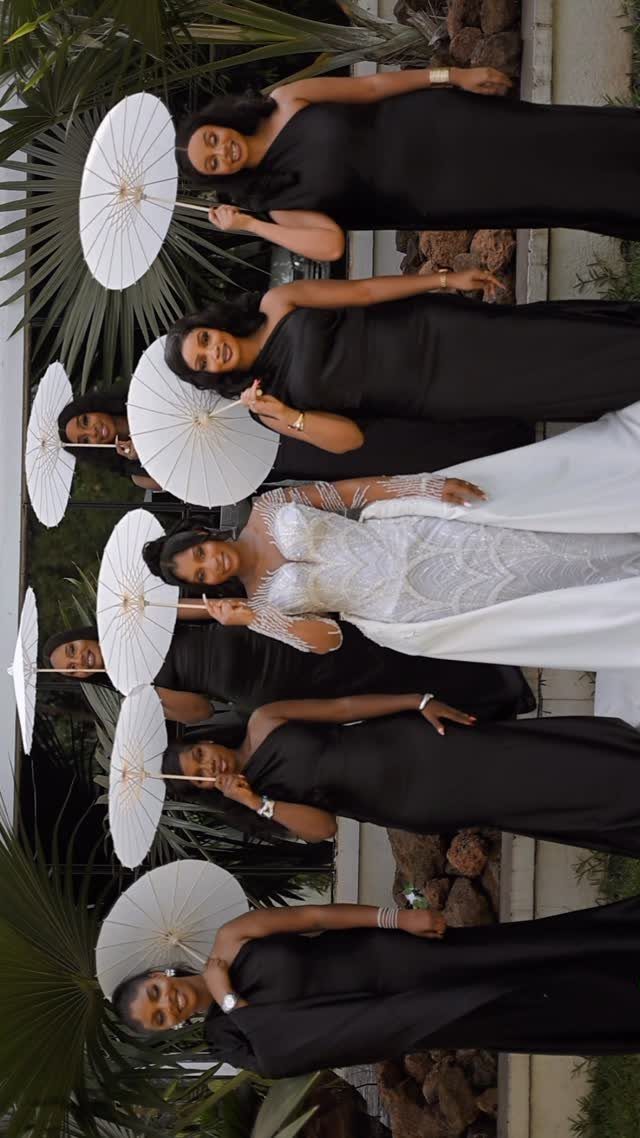 Bride in white lace gown with bridesmaids wearing long black gowns and white parasols