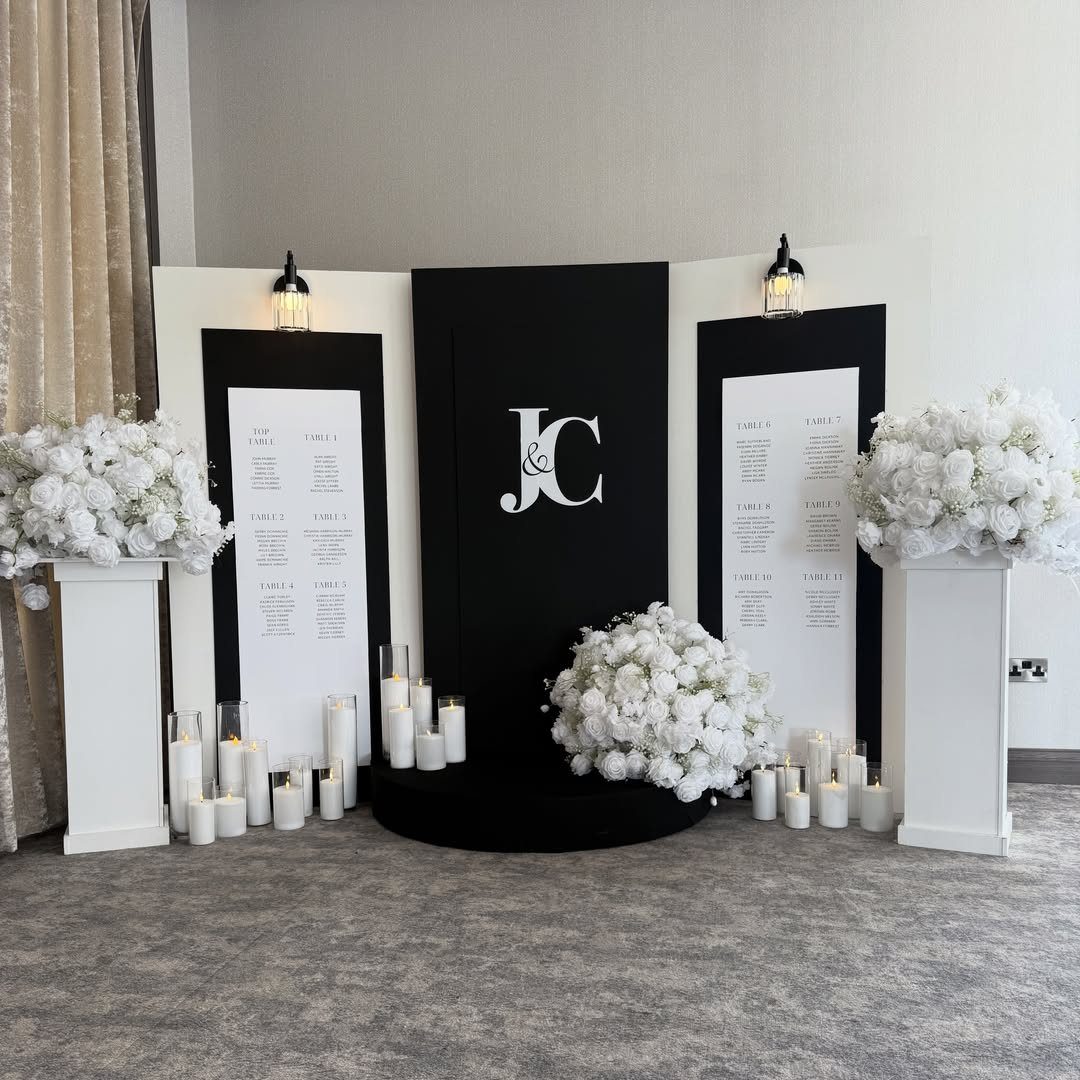 Black and white event backdrop with initials, seating charts, white flowers, and candles.