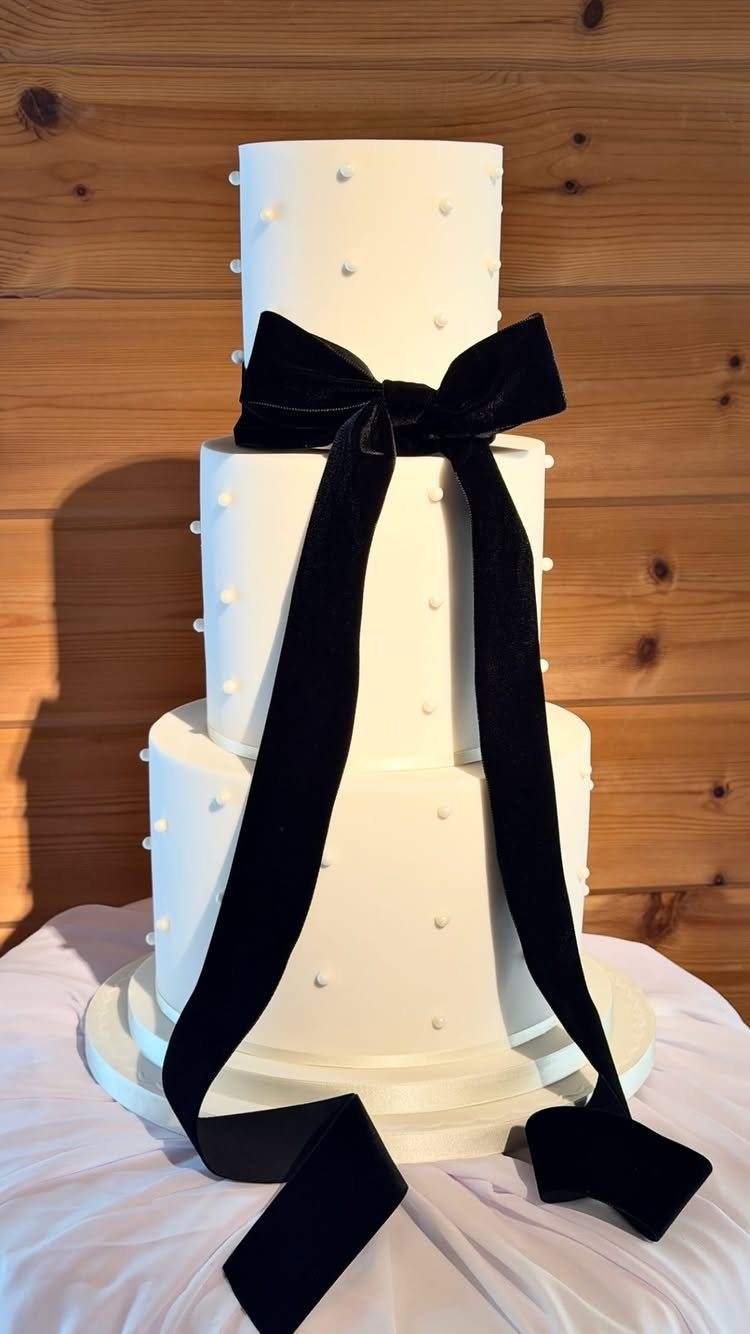 Three-tiered white wedding cake with small dots and a large black velvet bow.