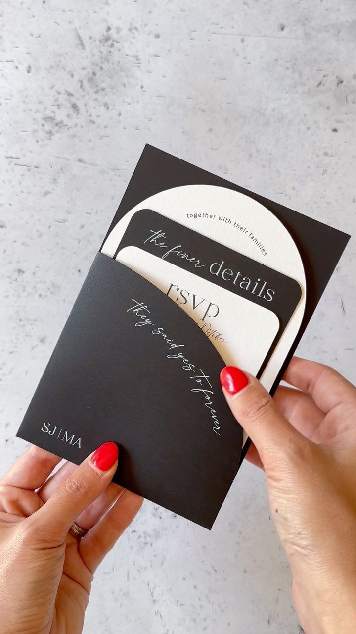 Black and white wedding invitation suite held by hands with red nail polish.