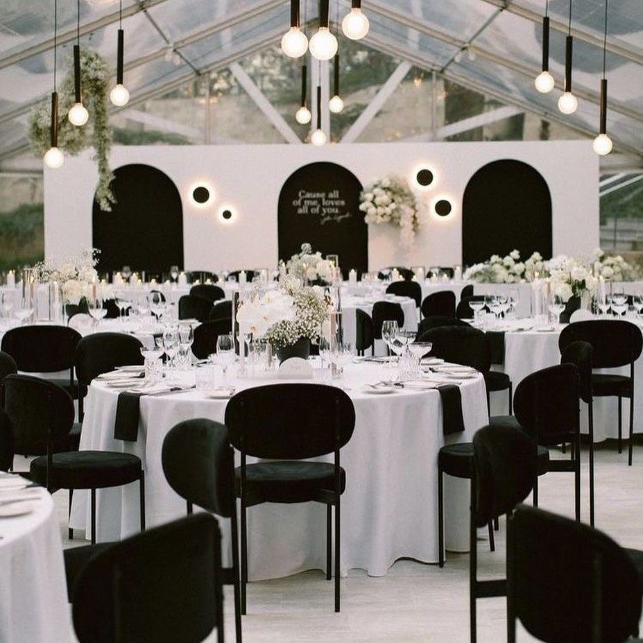 Round wedding tables with white linens, black napkins, and black chairs in a tent.