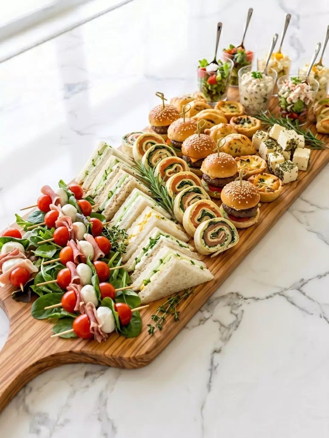 Assorted miniature appetizers and finger foods arranged on a long wooden serving board.