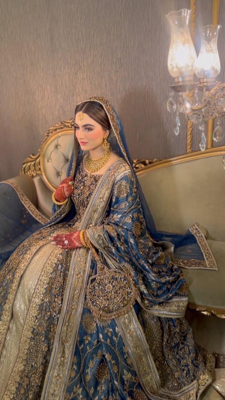 Woman in ornate blue and gold bridal lehenga sitting on a beige sofa