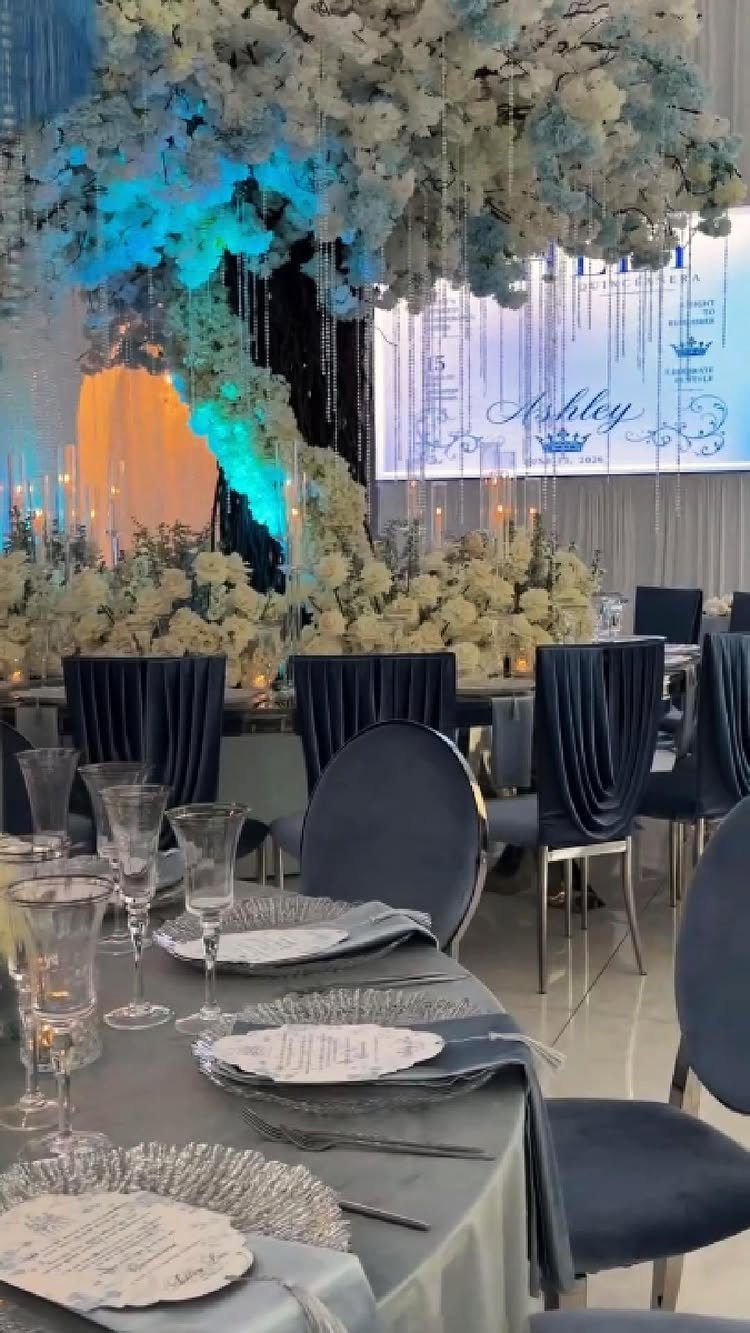 Wedding table with blue linens, clear glassware, and navy blue velvet chairs.