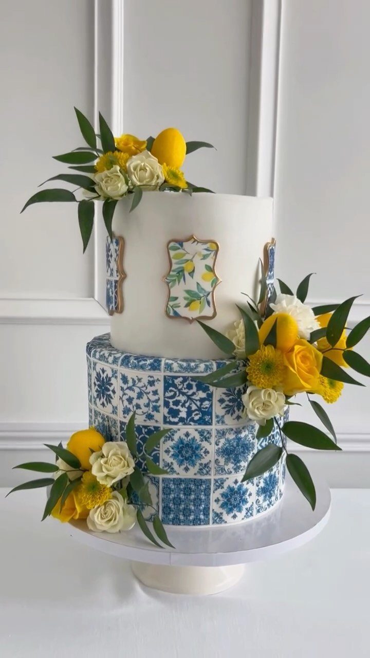 Two-tier wedding cake with blue tile patterns, yellow roses, and fresh lemons.