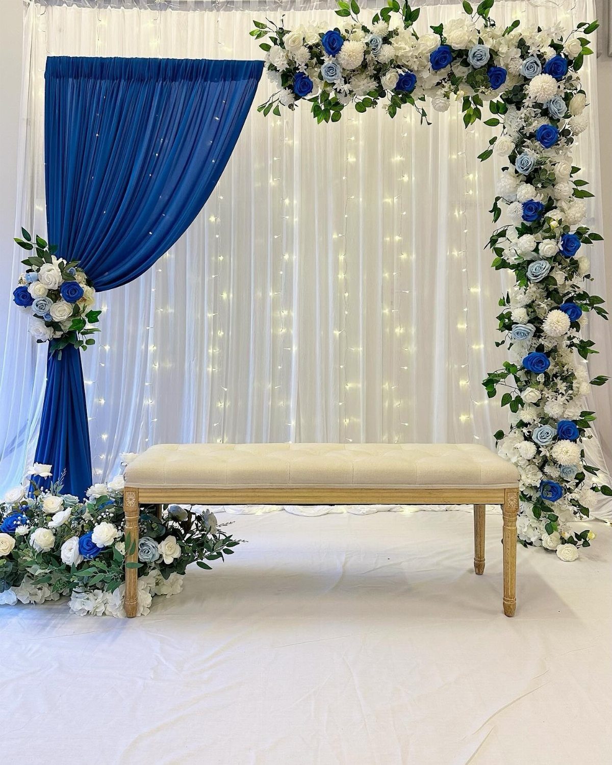 Blue and white floral arch with royal blue drapery and cream bench