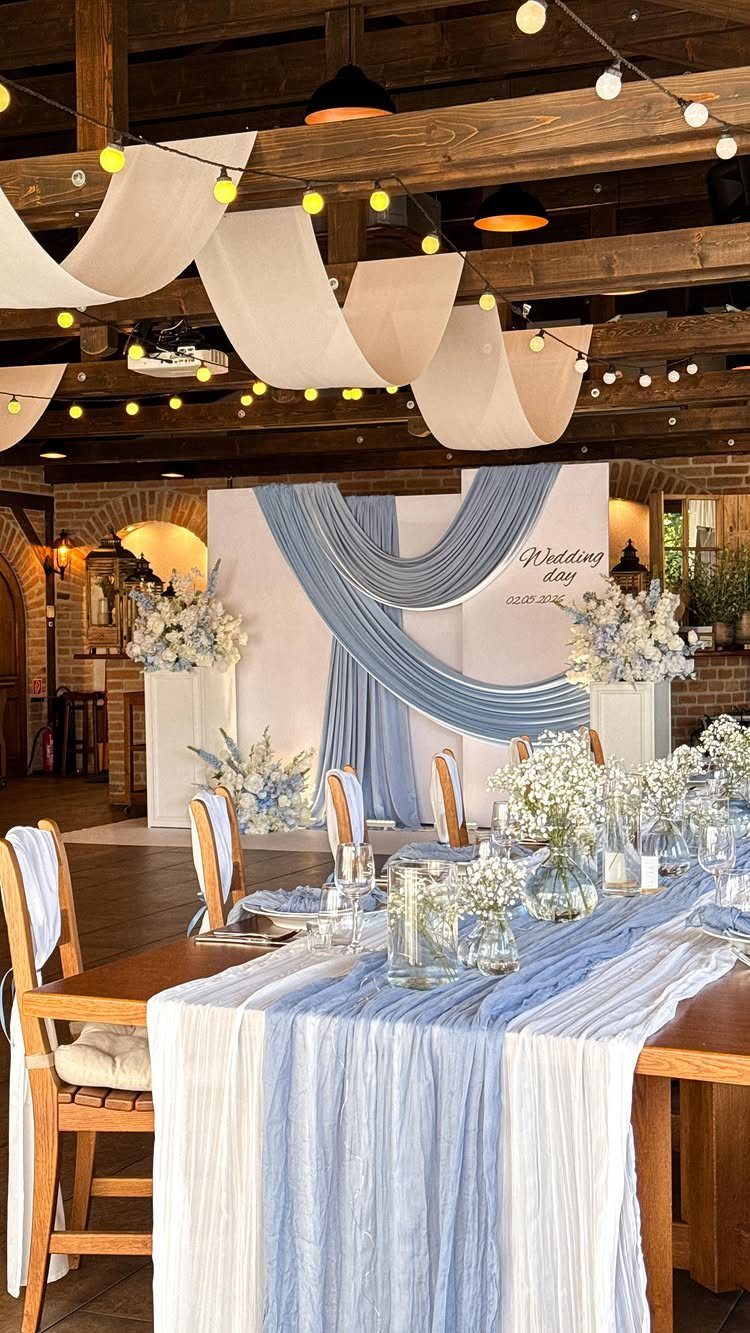 Wedding reception table with blue runners and a draped blue fabric backdrop.