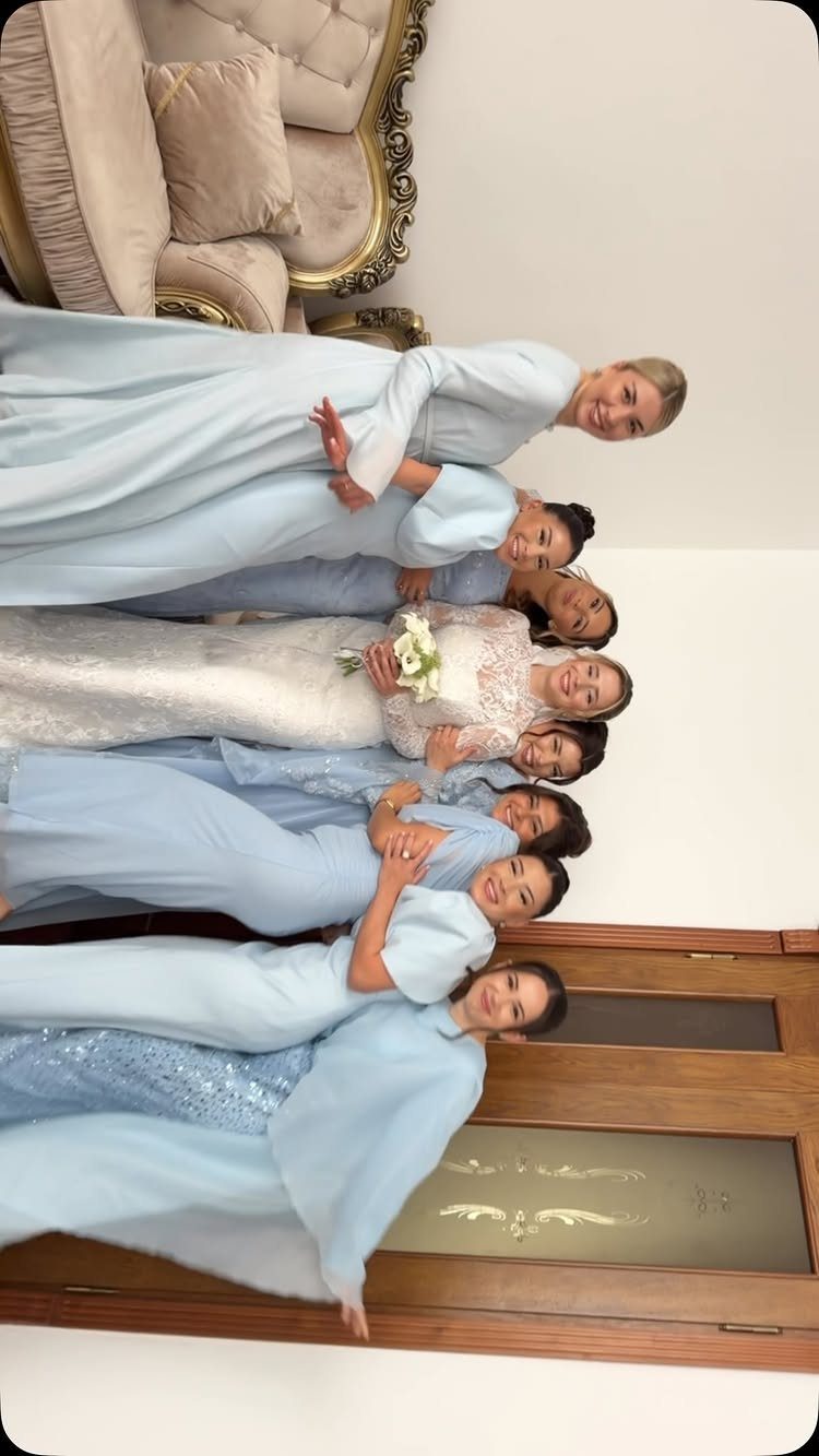 Bride in white lace dress surrounded by bridesmaids wearing light blue gowns.