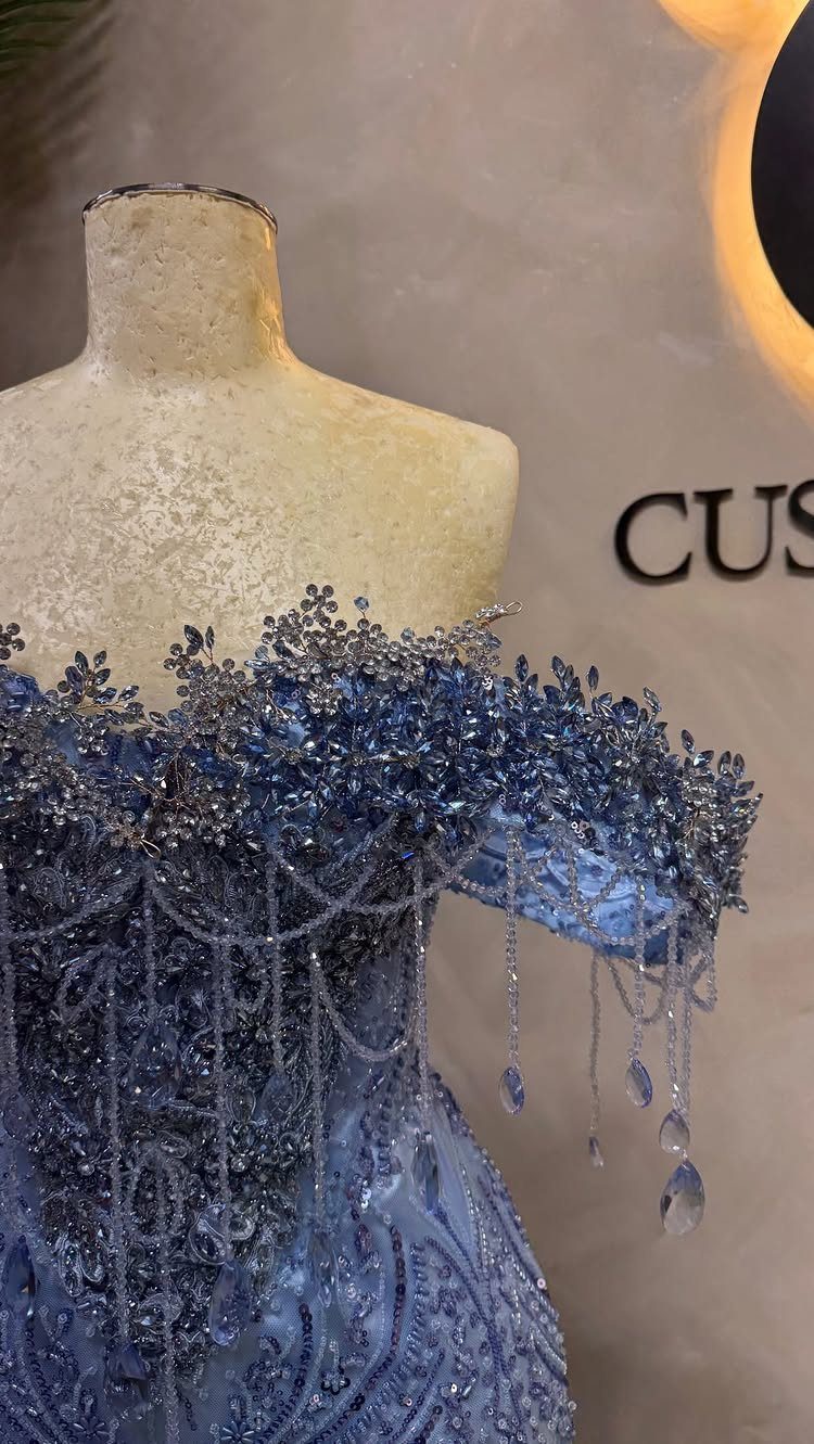 Blue beaded gown with crystal droplets displayed on a beige mannequin torso.