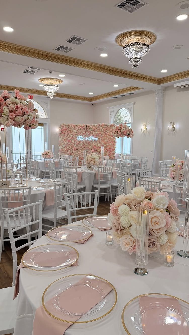 Wedding reception tables with blush pink floral centerpieces and gold-rimmed plates.