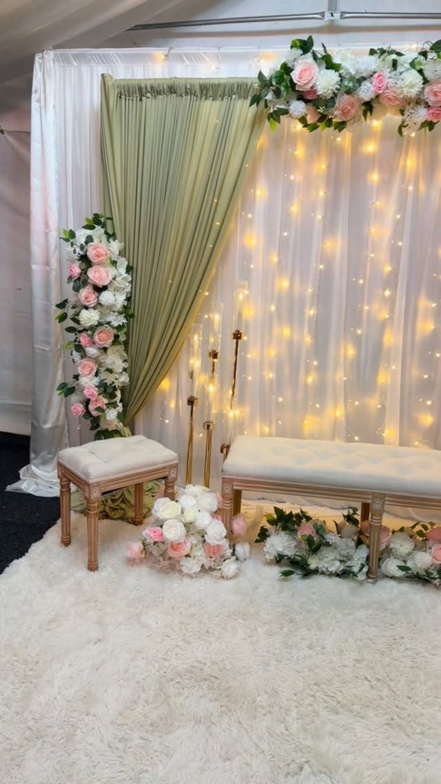 Wedding backdrop with sage green drapery, blush roses, and glowing fairy lights.