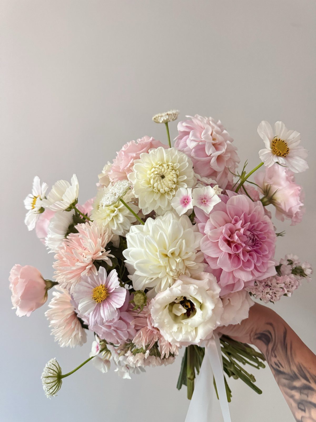 Blush and white wedding flower bouquet held by a tattooed hand.