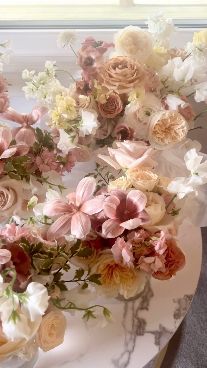 Dusty rose and mauve floral arrangement with cream roses on marble surface