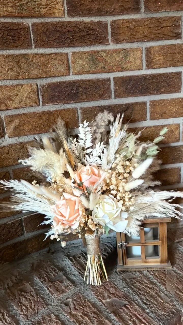 Dried floral bouquet with pampas grass and peach roses against a brick wall