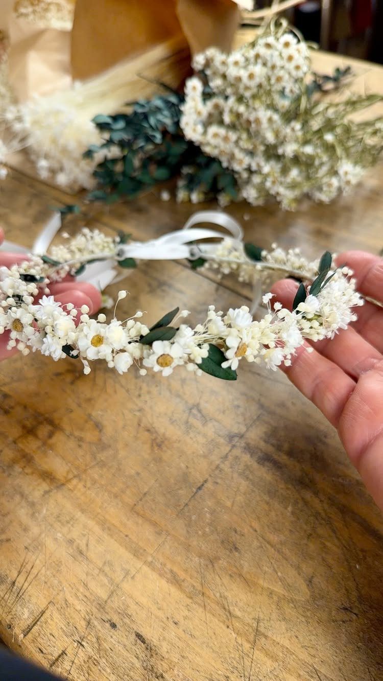 Flower crown made of small white blossoms held over a rustic wooden table.