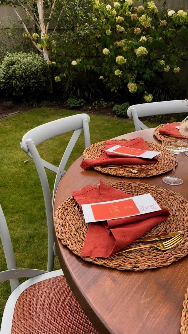 Wooden table set with woven rattan chargers and terracotta napkins in a garden.