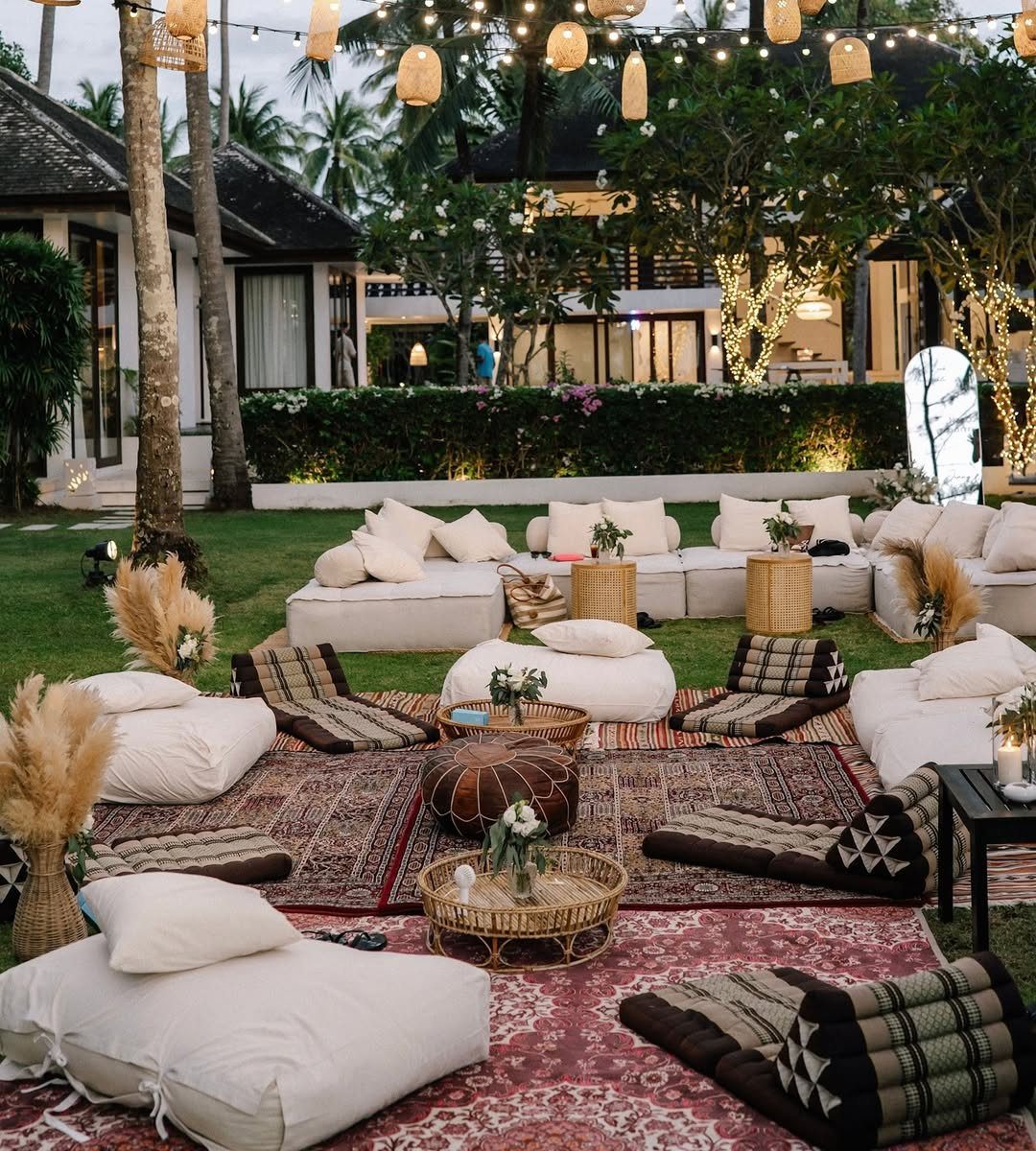 Outdoor lounge area with white bean bags, patterned cushions, and woven rugs under string lights.
