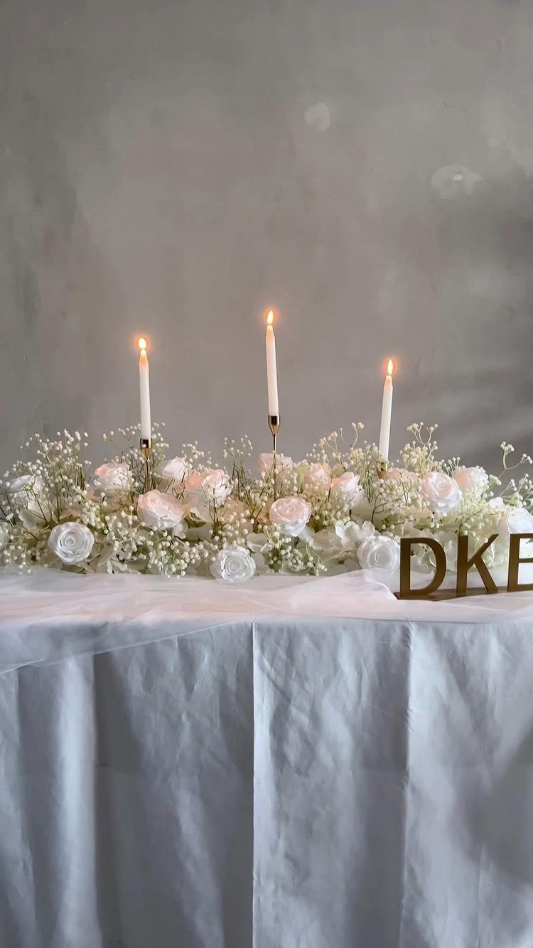 White roses and baby's breath centerpiece with lit taper candles on a table