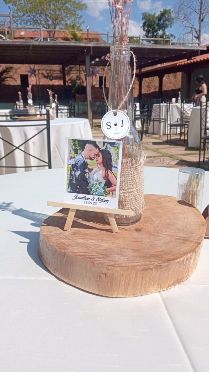 Wooden slice centerpiece with a burlap-wrapped bottle and a couple's photo on easel.