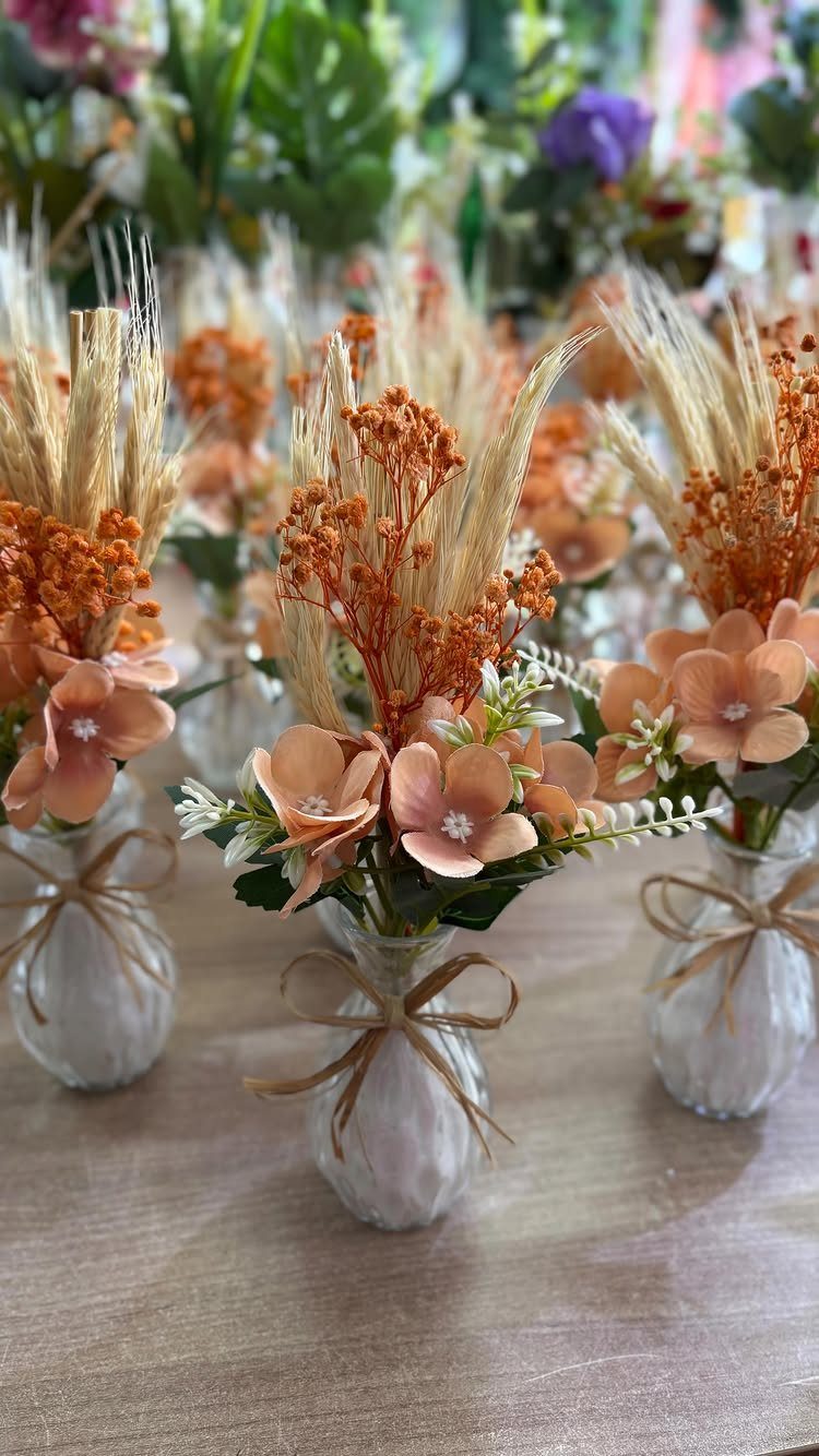 Dried orange flowers and wheat in small glass vases with brown ribbons.