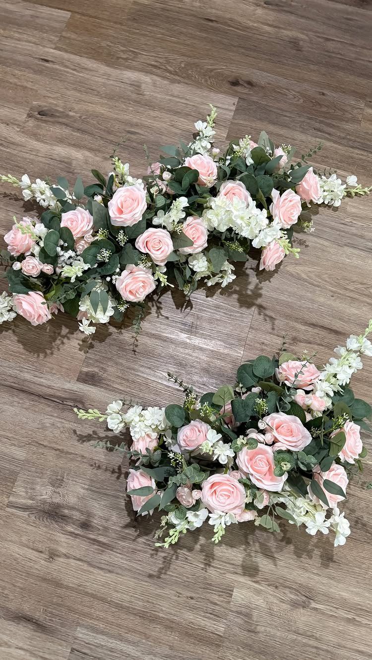 Pink roses and white flowers with greenery arranged in long table centerpieces.