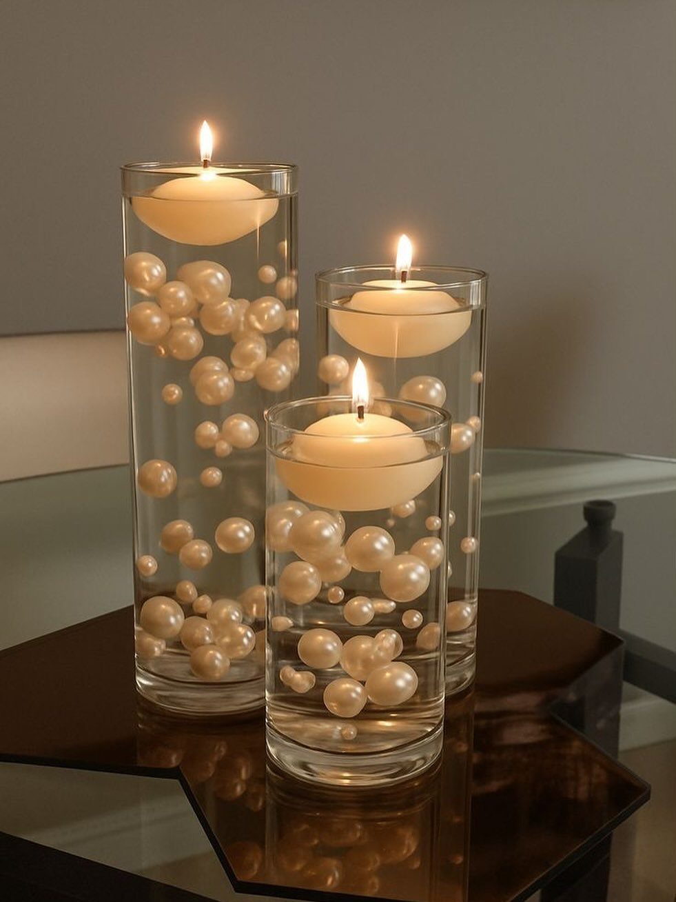 Three glass cylinder vases with floating white pearls and lit floating candles.