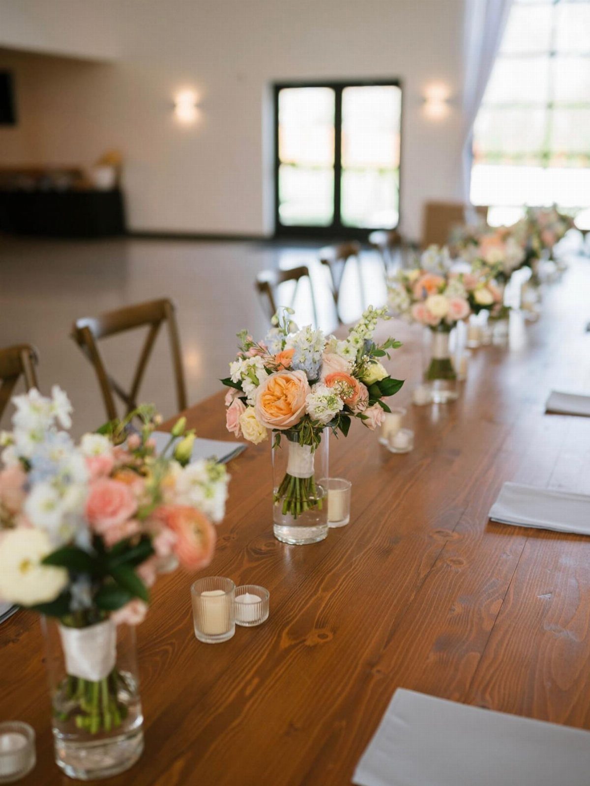 Floral centerpieces with peach and white flowers in glass vases on wooden table.