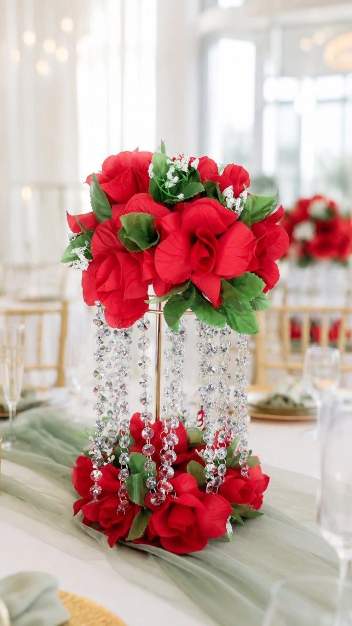 Red artificial rose centerpieces with crystal beads on a gold stand and green runner.