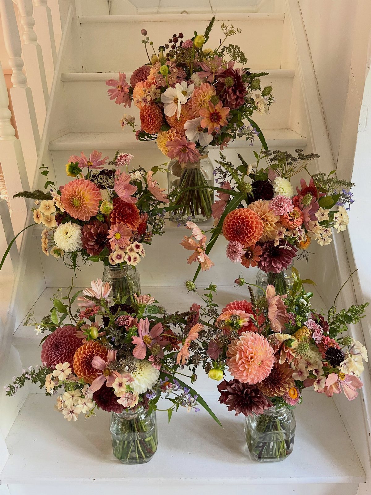 Colorful floral bouquets in mason jars arranged on white wooden stairs.