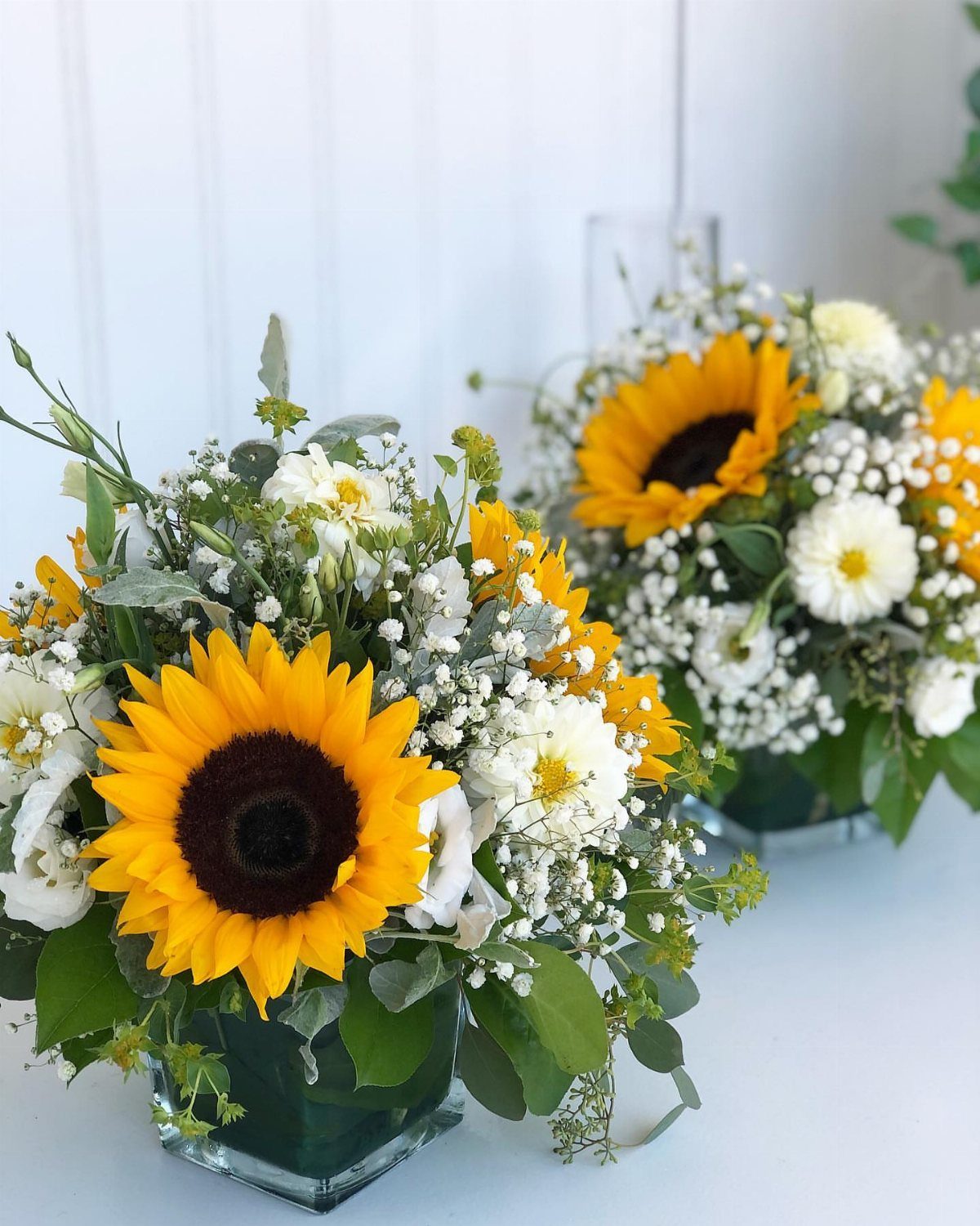 Sunflowers and white daisies in square glass vases as wedding table centerpieces.
