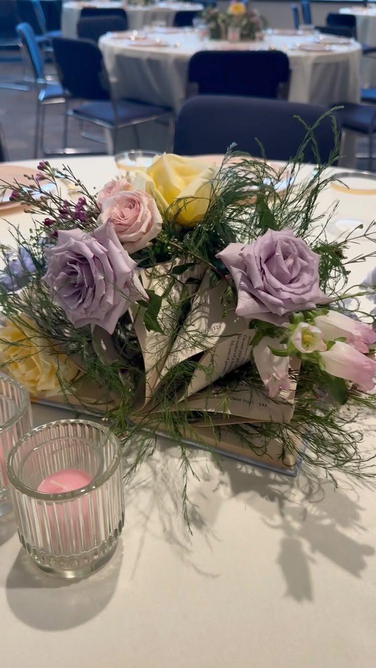 Open vintage book centerpiece with purple and yellow roses on a white table