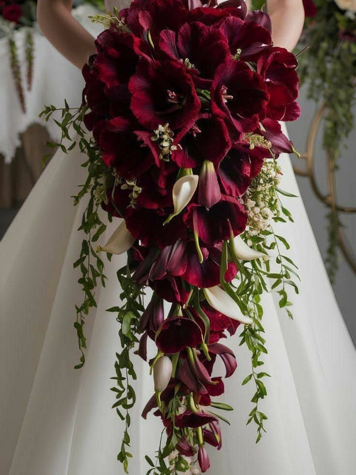 Cascading bridal bouquet with deep burgundy calla lilies and greenery against white dress