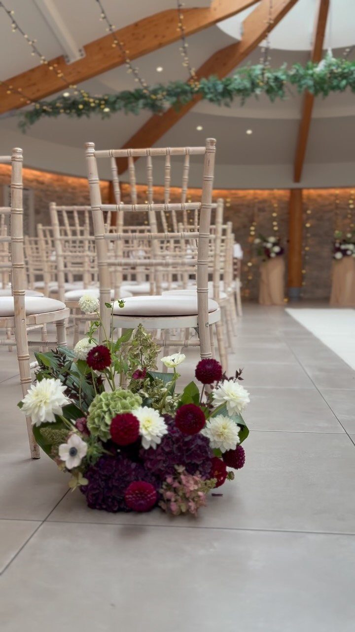 Burgundy and white flower cluster on a grey floor beside wedding chairs.