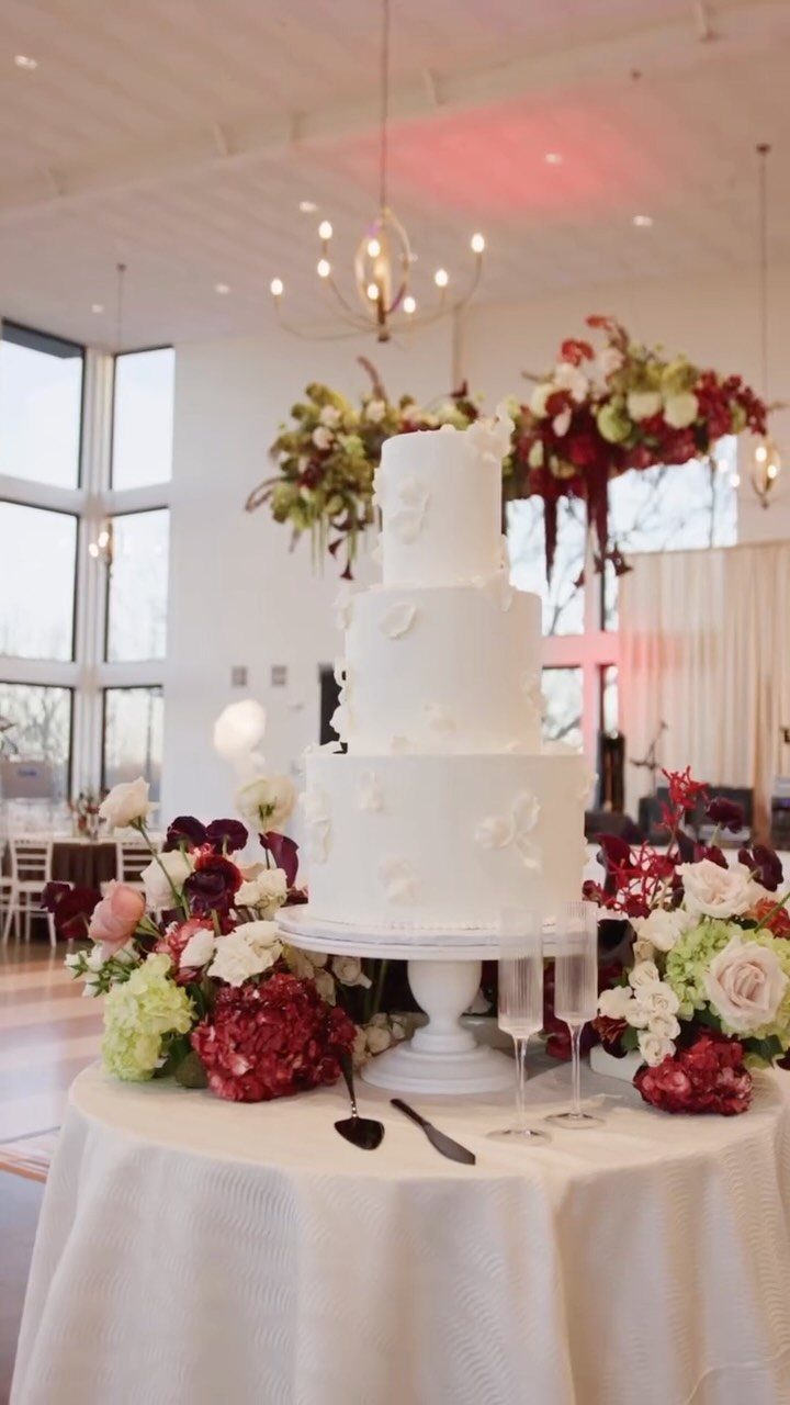 White wedding cake surrounded by burgundy flowers with hanging floral installations above