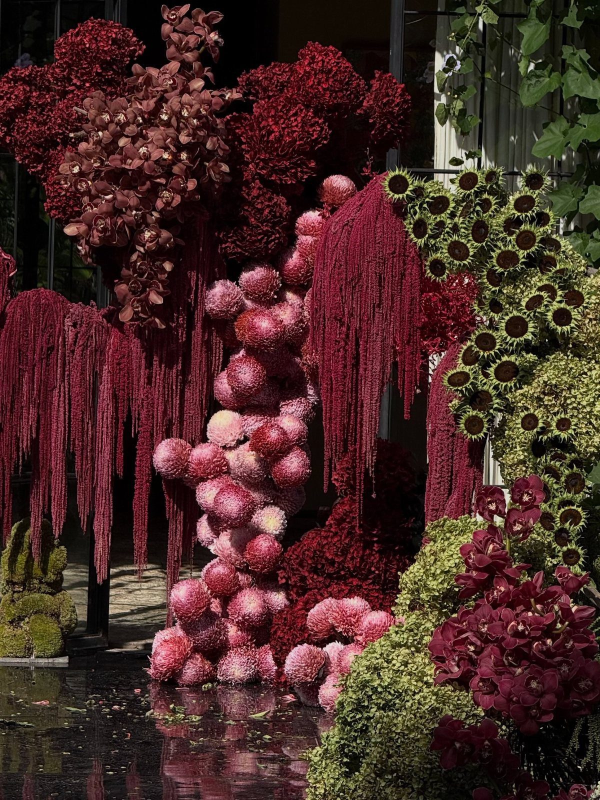 Burgundy and pink floral installation with trailing amaranthus and rounded flower clusters.