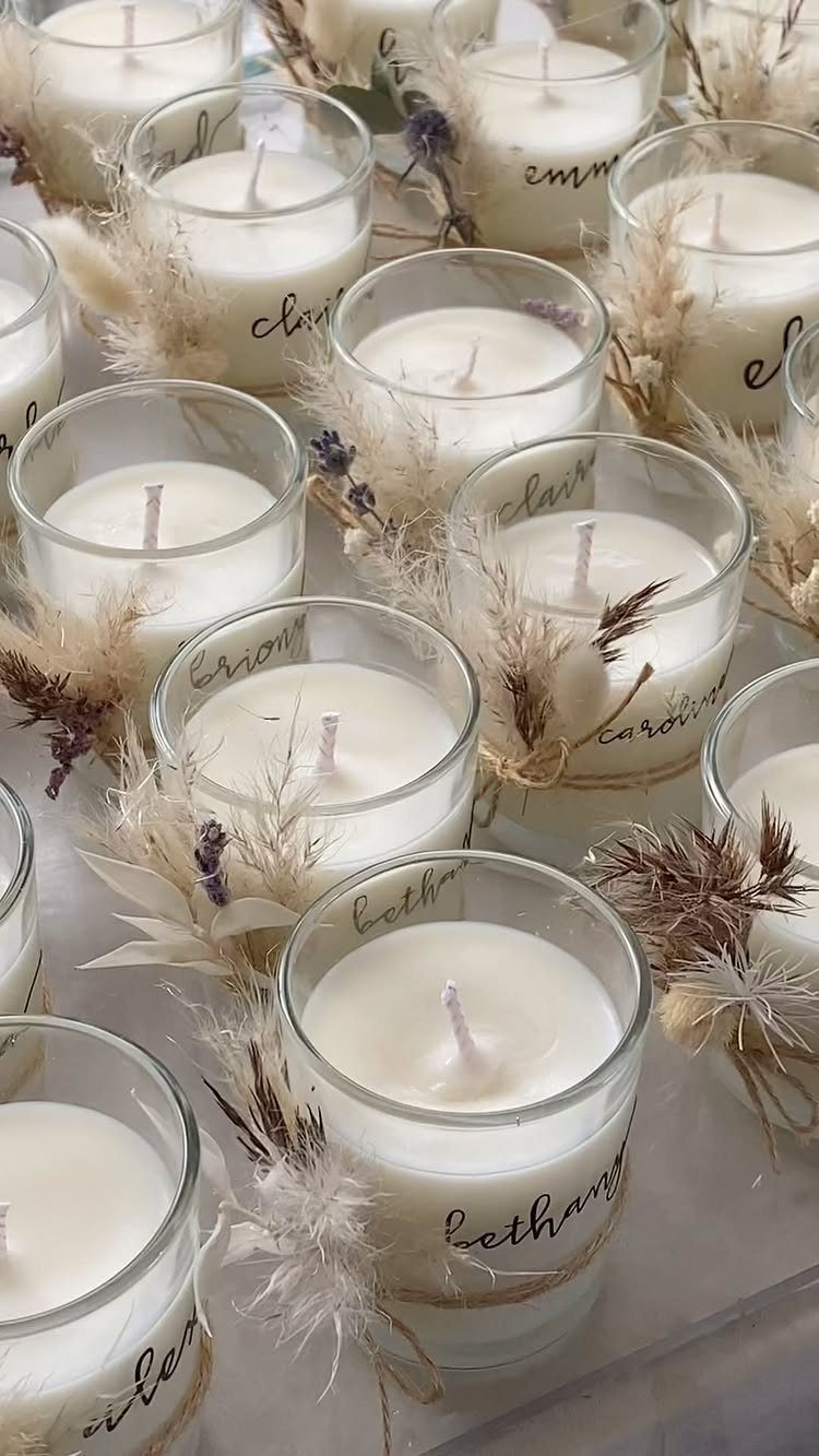 Small white candles in glass jars decorated with dried grass and cursive names.